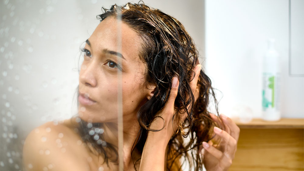 Woman behind the shower door in private bathroom performing hear washing