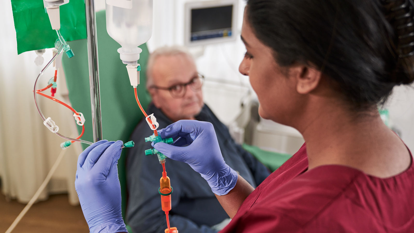 oncology-patient-with-glasses-sitting-on-the-chair-and-nurse-with-gloves-handling-cytoset-in-dayclinic